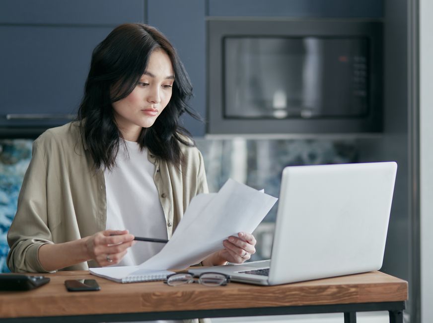 person reviewing tax documents on a laptop at a kitchen table