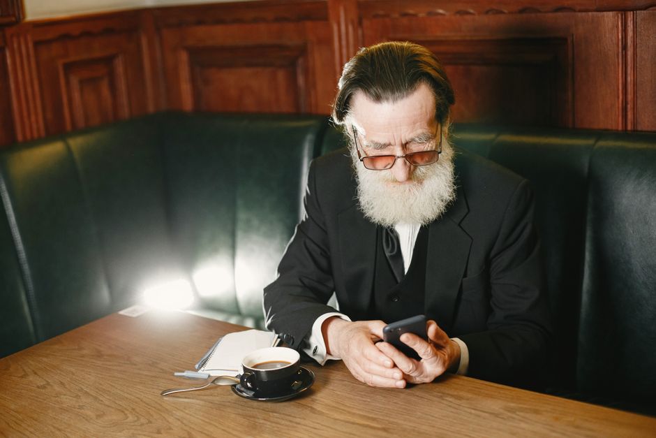 older adult reviewing a phone bill on a smartphone at the kitchen table
