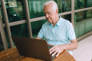 older adult using a laptop at the kitchen table to look up benefit programs