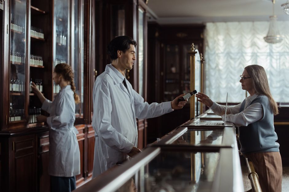Pharmacist checking a prescription and explaining discount pricing to a customer at the counter