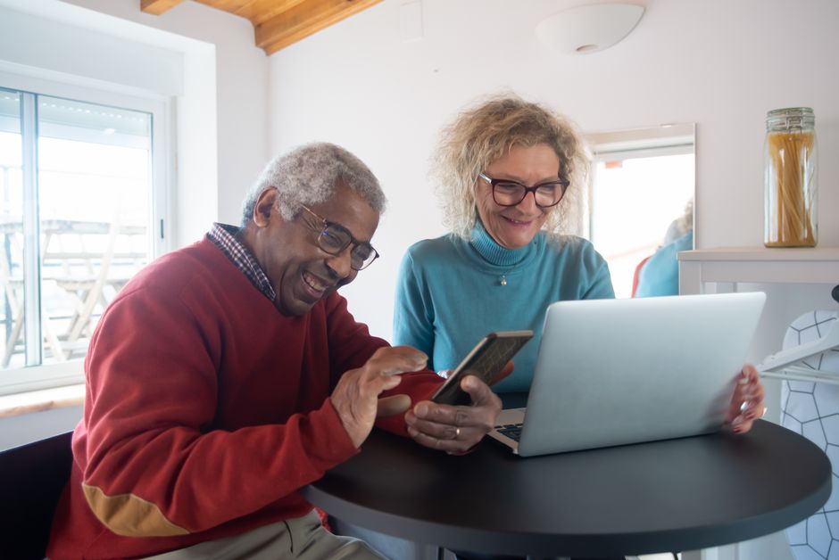 Senior couple checking a retirement budgeting app on a smartphone next to a laptop