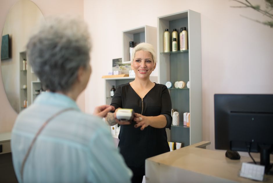 Senior customer showing ID at a hair salon checkout counter to receive a senior discount