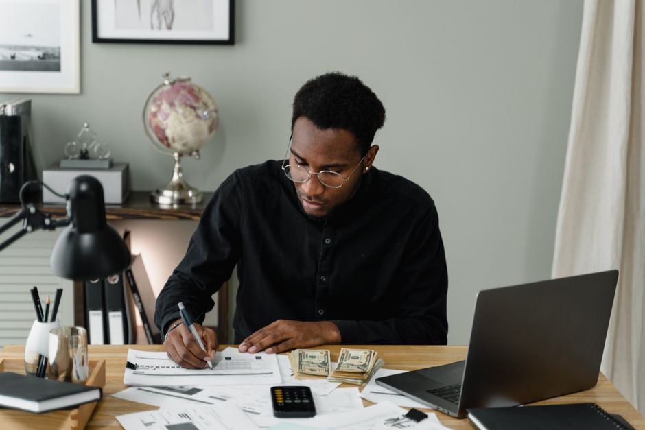Retired man using a laptop and calculator to compare renting versus owning costs at his kitchen table