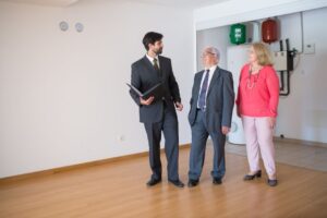Retired couple discussing whether to sell their home, standing next to a For Sale sign in the driveway