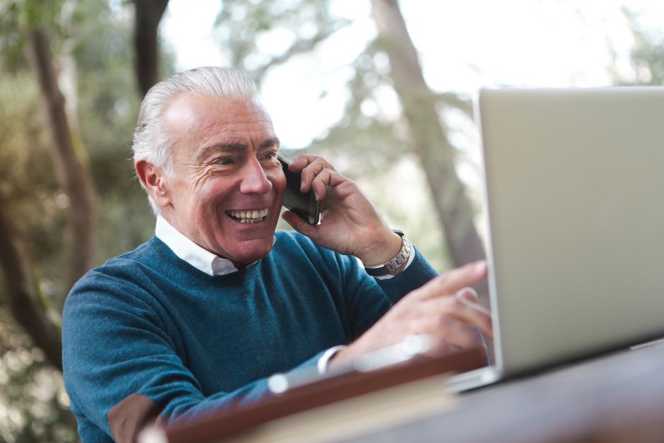 senior man comparing homeowners insurance quotes on a laptop while on the phone with an insurance agent