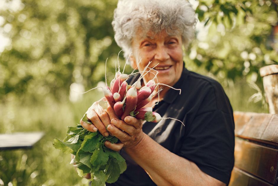 Senior woman gardening happily in the backyard of her own home, representing the comfort of homeownership in retirement