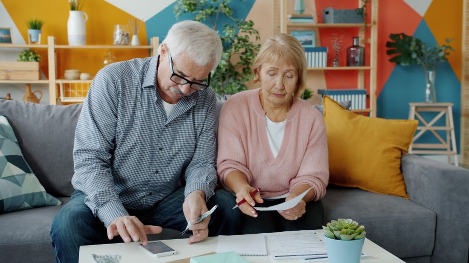 Retired couple reviewing financial documents and a calculator at home
